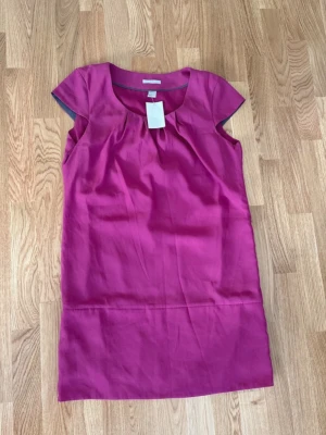Ny klänning H&M stl 38 - Snygg cerise kortklänning från H&M. Blusmaterial. Helt ny, prislappen kvar. Nypris 199 kr.