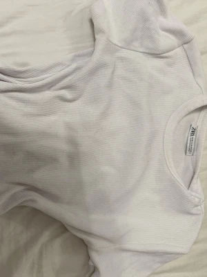 Vit ribbad t-shirt från Zara - Säljer en enkel och stilren vit ribbad t-shirt från Zara. T-shirten har korta ärmar och rund halsringning, perfekt till alla typer av outfits. Materialet är mjukt och stretchigt för en bekväm passform.