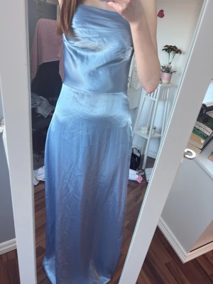 Ljusblå långklänning - Snygg ljusblå långklänning i glansigt material med axelbandslös design och figurnära passform. Klänningen har en enkel, elegant siluett och stängs med dragkedja i ryggen. Perfekt för speciella tillfällen när du vill sticka ut. (Pris går att diskutera) jag har sytt axelbandet för att det var för långt men det går att sprätta bort