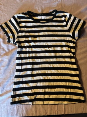 Randig svartvit t-shirt i bomull - Säljer en klassisk svartvit randig t-shirt med korta ärmar och rund hals. T-shirten är gjord i mjuk bomull och har en normal passform. Perfekt till jeans eller shorts för en enkel och stilren look.