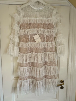 Vit spetsklänning med volanger - Säljer denna helt oanvända vita Carmine klänningen från Bymalina med spets och volanger. I storlek S. Dragkedja i bak vilket gör den lätt att ta på och av.  Nypris 2499kr. 