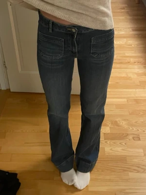Mörkblå bootcut jeans med fickor - Snygga mörkblå bootcut jeans med stora framfickor och markerade sömmar. Jeansen har normal hög midja och klassisk knappgylf. Perfekta för en avslappnad och trendig look. Aldrig använda!