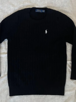 Svart stickad tröja Polo Ralph Lauren - Svart stickad tröja från Polo Ralph Lauren med klassisk kabelstickad design och broderad vit logga på bröstet. Rund halsringning och långa ärmar. Perfekt för dig som gillar stilrena och tidlösa plagg med premiumkänsla. Skriv vid minsta fundering och priset går att diskutera👍✅🤝