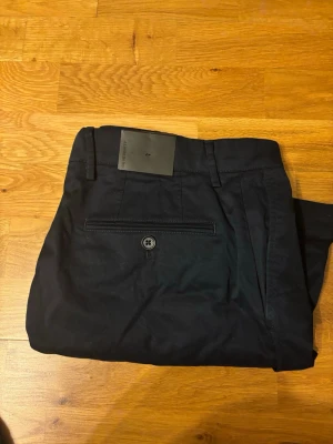 J. Lindeberg Nathan Cloud Satin Shorts - OBS ALDRIG ANVÄNDA - LAPPEN SITTER PÅ. Snygga mörkblå shorts från J. Lindeberg klassisk modell. Tillverkade i bomull med normal passform, bälteshällor och knappstängning bak. Perfekta för en stilren och avslappnad look under varmare dagar.