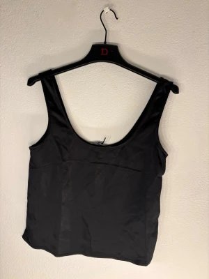 Svart linnetopp i satin - Aldrig använd, då den är förstor för mig. Nypris 299kr. Stilren svart linnetopp i glansigt satinmaterial med breda axelband och rundad urringning både fram och bak. Perfekt att matcha med jeans eller kjol för en trendig look.