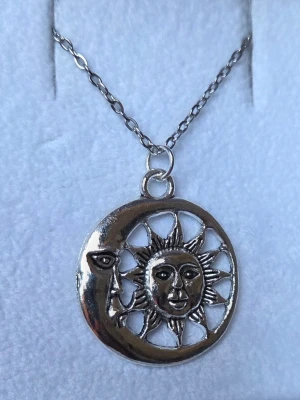 Halsband med sol och måne hänge - Snyggt halsband i silverfärgad rostfritt stål med ett runt hänge som föreställer en halvmåne med ansikte och en sol i mitten. Kedjan är tunn och har klassisk länkdesign, 45 cm. Perfekt accessoar för dig som gillar mystiska och unika smycken. Hänget är ca 2,5-3 cm.