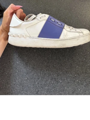 Vita valentino opens med blå lila design - Snygga vita sneakers från Valentino med en bred lila remsa över mitten och nitar på hälen. Skorna har klassisk låg profil och är tillverkade i läder med gummisula. Perfekta för dig som vill ha en unik touch på din outfit. Har boxen till fråga, kan skicka fler bilder vid önskan