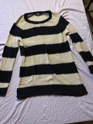 Randig stickad tröja svart och beige - Stickad tröja med breda svarta och beige ränder. Tröjan har rund halsringning, långa ärmar och ribbstickade muddar vid ärmslut och nederkant. Perfekt för dig som gillar en avslappnad och stilren look.