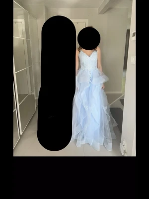 Ljusblå långklänning med spetsdetaljer - Elegant ljusblå långklänning med v-ringad spetsliv och tunna axelband. Kjolen har flera lager av volangigt tylltyg och fina spetsapplikationer. Perfekt för bal eller student. Klänningen har en romantisk och drömmig känsla. Skriv för fler frågor och mått! Använde bara 1 gång så inga defekter, verkligen superfin 