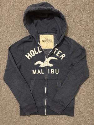 Vintage Hollister Zip-Hoodie - Sjukt fet Hollister zip hoodie som är mycket eftertraktad | Mycket bra skick, snören fattas | Storlek S | Längd ≈ 64cm , Bredd armhåla-armhåla ≈ 54cm | Modell 175cm, 68kg | Hör av vid funderingar!