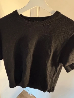 Svart stickad kortärmad topp - En enkel och stilren svart stickad topp med rund hals och korta ärmar. Perfekt att matcha med jeans eller kjol för en clean look. Mjuk och bekväm.