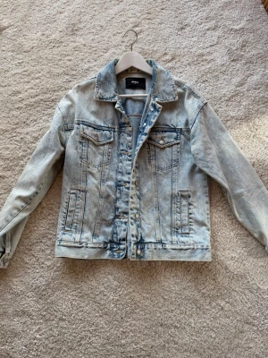 Ljusblå oversized jeansjacka - Säljer en ljusblå jeansjacka från BikBok med klassisk krage, knappstängning och två bröstfickor med lock. Jackan har en oversized passform och cool tvättad look som ger en avslappnad vibe. Perfekt att slänga över en hoodie eller t-shirt. Knappt använd. 