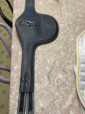 Svart magplatta i läder - Säljer en svart magplatta i läder med vita sömmar och dekorativa detaljer. Plattan har flera fästen och spännen, perfekt för hästutrustning. Passar till sadel och ger extra skydd vid hoppning. Endast använd 2 gånger, nypris ca 900kr. 135 cm