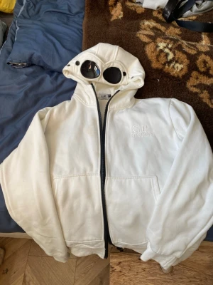 C.P. Company hoodie - Säljer en vit hoodie från C.P. Company med ikoniska inbyggda goggles i huvan. Denna hoodie är väldigt skön att ha på sig och säljer denna pga ny stil. Den passar S och Xs perfekt 