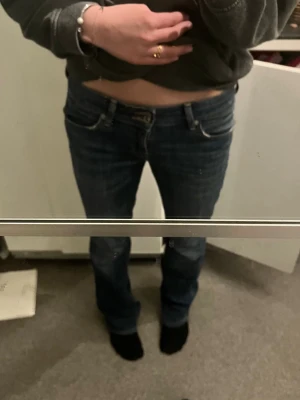 Mörkblå bootcut jeans - Säljer ett par mörkblå bootcut jeans med klassisk femficksdesign och låg midja. Jeansen har snygga slitningar och kontrastsömmar. 