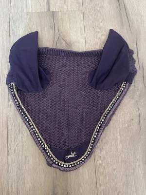 Lila huva till häst  - Snygg lila huva med lite bling. I storlek full, med elastiskt tyg i öronen.. Den är nytvättad och som ny! Köpt på granngården för ett tag sen, minns inte vad det är för märke! 