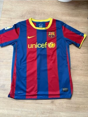 FC Barcelona matchtröja Nike L - Säljer en klassisk FC Barcelona matchtröja från Nike i storlek L. Tröjan har blå och röda vertikala ränder, gula detaljer och klubbmärke på bröstet. Tillverkad i Dri-Fit material som andas, perfekt för fotbollsträning eller match.