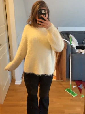 Vit fluffig stickad tröja - Mysig vit stickad tröja med fluffig textur och avslappnad passform. Tröjan har långa ärmar och rund halsringning, perfekt för att hålla värmen under kyliga dagar. Passar till både jeans och kjol för en trendig look.