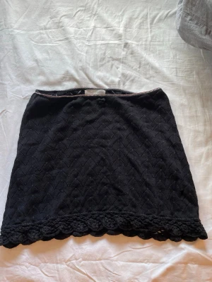 Svart spetskjol från Odd Molly - Supersöt svart kortkjol från Odd Molly med spetsdetaljer och vågig kant nertill. Kjolen har ett diskret mönster och är perfekt för dig som gillar en feminin och stilren look. Passar till många olika outfits och är lätt att matcha.