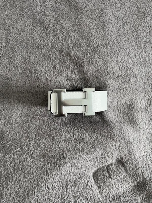 Herme’s bälte  - Stilrent vitt skärp med ett stort, silverfärgat H-format spänne. Skärpet har en slät yta och är perfekt för att lyfta din outfit med en modern touch. Passar till både jeans och kostymbyxor.