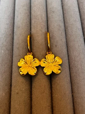 Guldpläterade örhängen med blomma - Snygga örhängen i guldpläterad metall med hängande blommor i form av fyrklöver. Perfekta för att ge din look en söt och trendig touch. Blommorna har fina detaljer och örhängena är lätta att bära.
