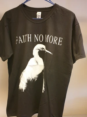 Faith No More svart t-shirt XL - Svart t-shirt från Fruit of the Loom med stort vitt tryck Faith No More på bröstet. Klassisk rund hals och korta ärmar. Perfekt för dig som gillar bandmerch och vill sticka ut med en cool printad tee.