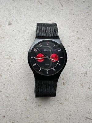 Bering Titanium Watch 39 mm - (OBS. LÄS ANNONS INNAN KÖP!)  Stilren Bering Titanium-armbandsur med svart mesharmband och röda detaljer på urtavlan. Modellen har safirglas som är reptåligt och i mycket fint skick utan synliga repor. Själva klockan och armbandet har däremot en del skavanker/repor från användning.  Jag vet tyvärr inte om armbandsuret fungerar eftersom visarna inte rör sig. Vet ej om det endast behövs batteribyte eller annan service, därav det låga priset. Säljs därför som otestad. 