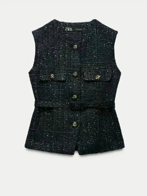 Svart tweedväst från Zara - Stilren svart tweedväst från Zara med glittriga detaljer och dekorativa guldknappar framtill. Västen har två fickor med lock och markerad midja för en snygg siluett. Perfekt för att lyfta din outfit med en trendig touch.