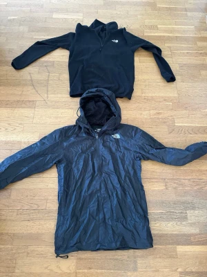 Svarta hoodies från The North Face - Två svarta hoodies från The North Face, en klassisk sweatshirt med huva och en tunnare, vind- och vattenavvisande hoodie med dragkedja och justerbar huva. Perfekt för dig som gillar stilren design och funktionella material.
