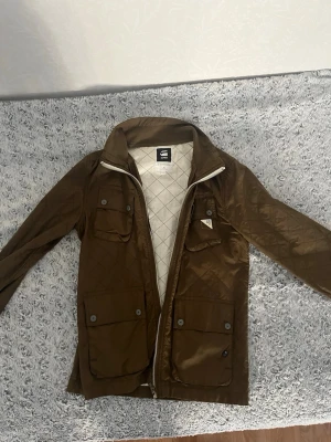 G-star jacka priset kan diskuteras! - Snygg brun quiltad jacka från G-Star RAW med fyra framfickor och dragkedja. Jackan har lång ärm, ståkrage och ett rutigt innerfoder. Perfekt för dig som gillar stilren och funktionell design.