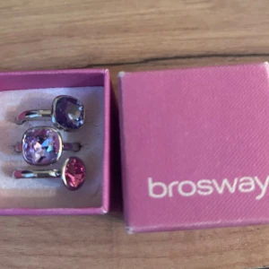 Brosway ringar med färgade stenar - Två stilrena ringar från Brosway med stora, gnistrande stenar i lila och rosa nyanser. Ringarna har en modern, silverfärgad bas och levereras i originalask. Perfekt för dig som gillar att sticka ut med färgglada accessoarer.