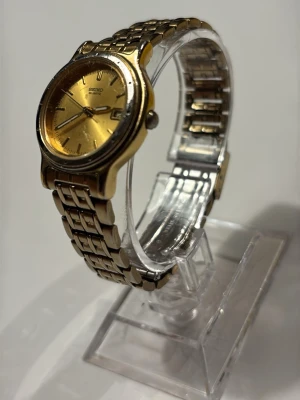 Guldfärgad Seiko Quartz klocka - Stilren guldfärgad klocka från Seiko med klassisk länkarmband i metall. Urtavlan är guldig med datumvisning och tydliga markeringar. Perfekt accessoar för dig som gillar tidlös design och elegans.
