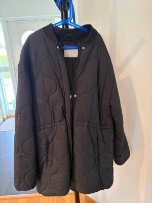 Svart quiltad pufferjacka - Säljer en svart quiltad pufferjacka med rundad krage och dragkedja framtill. Jackan har två stora fickor och ett vågigt mönster i vadderingen som ger en cool look. Perfekt för kalla dagar och riktigt skön att bära.
