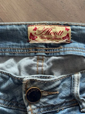 Ljusblå jeans från Alcott - Säljer ett par ljusblå jeans från Alcott Vintage Denim med snygga detaljer som dragkedja på fickan och mörkblå knapp framtill. Klassisk femficksmodell i mjuk denim med kontrastsömmar. Perfekta för en cool och trendig look.