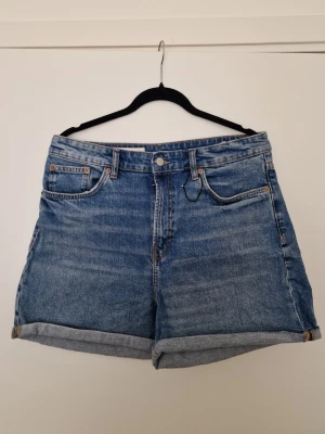 Zara Blå jeansshorts med upprullad kant - Klassiska Zara blå jeansshorts med fem fickor och upprullad kant. Shorts i rak modell med knapp- och dragkedjestängning, tillverkade i denim. Perfekta för en avslappnad och trendig look. Aldrig använd, bara tvättad en gång. Storlek 44. 