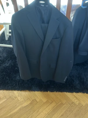Svart kavaj från Selected Homme - Stilren svart kavaj från Selected Homme med två knappar framtill, klassisk krage och tre fickor. Kavajen har slät finish och helfodrad insida för extra komfort. Perfekt för en dressad look och enkel att matcha med skjorta eller t-shirt.