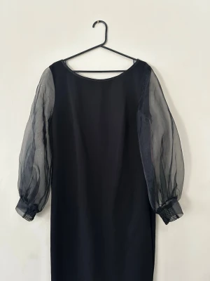 Svart klänning med transparenta ärmar - Ny Stilren svart klänning med rund halsringning och långa, transparenta ballongärmar i mesh. Klänningen har en rak passform och diskreta muddar vid ärmsluten. Perfekt för dig som gillar en enkel men trendig look. Nypris 2499 