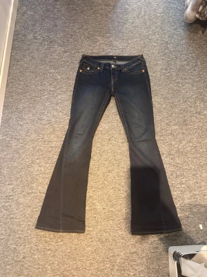 Mörkblå bootcut jeans True Religion joey - Säljer ett par mörkblå bootcut jeans från True Religion med klassiska snygga fickdetaljer bak.💕(andvänts ett få tal gånger) storlek:w26