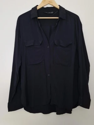 Svart skjorta med fickor från Zara - Stilren svart skjorta från Zara med två bröstfickor och klassisk krage. Skjortan har lång ärm och knäppning framtill. Perfekt för dig som gillar en enkel men snygg look. Storlek XXL. Fint skick