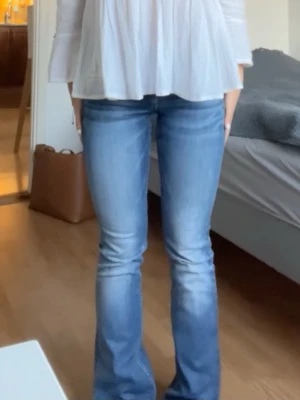 Blå bootcut jeans med utsvängda ben - Snygga blå bootcut jeans med lätt utsvängda ben och klassisk femficksmodell. Jeansen har en ljus tvätt och är tillverkade i denim. Perfekta för dig som gillar en retroinspirerad look och vill ha ett par jeans som sticker ut lite extra. Midje: 35 och innebenslängd: 73