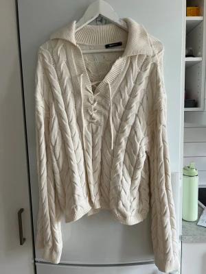 Vit kabelstickad tröja Gina Tricot - Säljer en vit kabelstickad tröja från Gina Tricot med krage och snörning vid halsen. Tröjan har långa ärmar och ribbade muddar. Perfekt för kalla dagar och riktigt mysig att ha på sig.