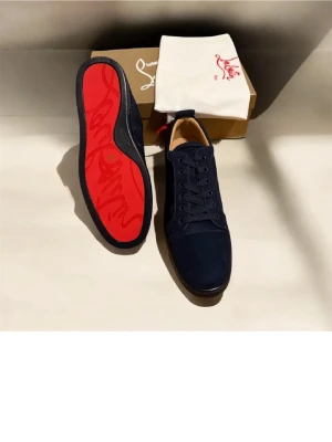 Mörkblå sneakers från Christian Louboutin - Snygga mörkblå sneakers från Christian Louboutin med klassisk röd sula och ovandel i mocka. Skorna har rund tå, svarta skosnören och diskreta detaljer. Perfekta för dig som vill ha en stilren och lyxig look med en ikonisk touch. Med box. De är använda en vecka men väldigt fint skick.