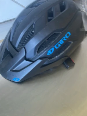 Svart cykelhjälm från Giro - Säljer en svart cykelhjälm från Giro med blå logotyp och flera ventilationshål. Hjälmen har justerbart spänne och MIPS-skydd för extra säkerhet. Tillverkad i tålig plast med skuminsida för komfort.Finns lite små märken på några ställen därav billigare pris 