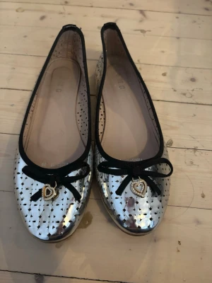 Silvriga ballerinaskor med hjärtdetalj - Säljer söta silvriga bellerinaskor, detta på grund av att de är för små för mig, jag skulle säga att det är en smal 39. Köpte på Vinted men har aldrig använt själv. Har en liten defekt som syns på sista bilden. Pris kan diskuteras. 
