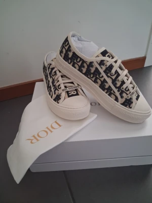 Dior Oblique låga sneakers - Snygga Dior Oblique sneakers i canvas med klassiskt blått och vitt monogrammönster. Skorna har vita snören, gummisula och diskreta Dior-detaljer på sidan och hälen. Perfekta för dig som vill ha en lyxig och trendig look.