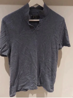 Blå kortärmad topp från Riley - Snygg blå topp från Riley med korta ärmar och unik krage med liten v-ringning. Tillverkad i mjuk bomull, perfekt för en avslappnad och stilren look. Enkel att matcha med jeans eller shorts.
