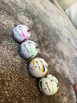 TaylorMade golfbollar med färgstänk - Fyra vita golfbollar från TaylorMade med unika färgstänk i rosa, grön, gul och svart. Bollarna har klassisk rund form och är tillverkade i slitstarkt material. Perfekta för dig som vill sticka ut på golfbanan. Skriv privat för pris