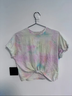Pastell tie-dye t-shirt med knut - En kortärmad t-shirt i pastellfärgat tie-dye-mönster med en snygg knut framtill. T-shirten har en lös passform och är tillverkad i mjuk bomull, perfekt för en chill och trendig look.