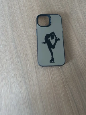 Grått mobilskal med konståkare - Snyggt grått mobilskal från Spigen med svart siluett av en konståkare på baksidan. Skalets design är stilren och skyddar mobilen samtidigt som det ger en sportig vibe. Passar perfekt för dig som gillar konståkning eller vill ha ett unikt motiv på mobilen. iPhone 15