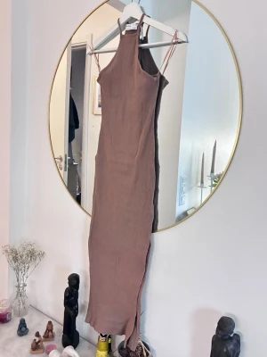 Beige ribbad långklänning från Gina Tricot - Trendig beige långklänning från Gina Tricot med smala axelband och hög halsringning. Klänningen är ribbad och har en kroppsnära passform som framhäver siluetten. Perfekt för dig som gillar minimalistisk och stilren design.